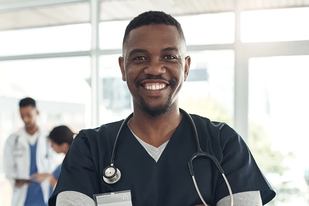 A man wearing black scrubs with a stethoscope around his neck.